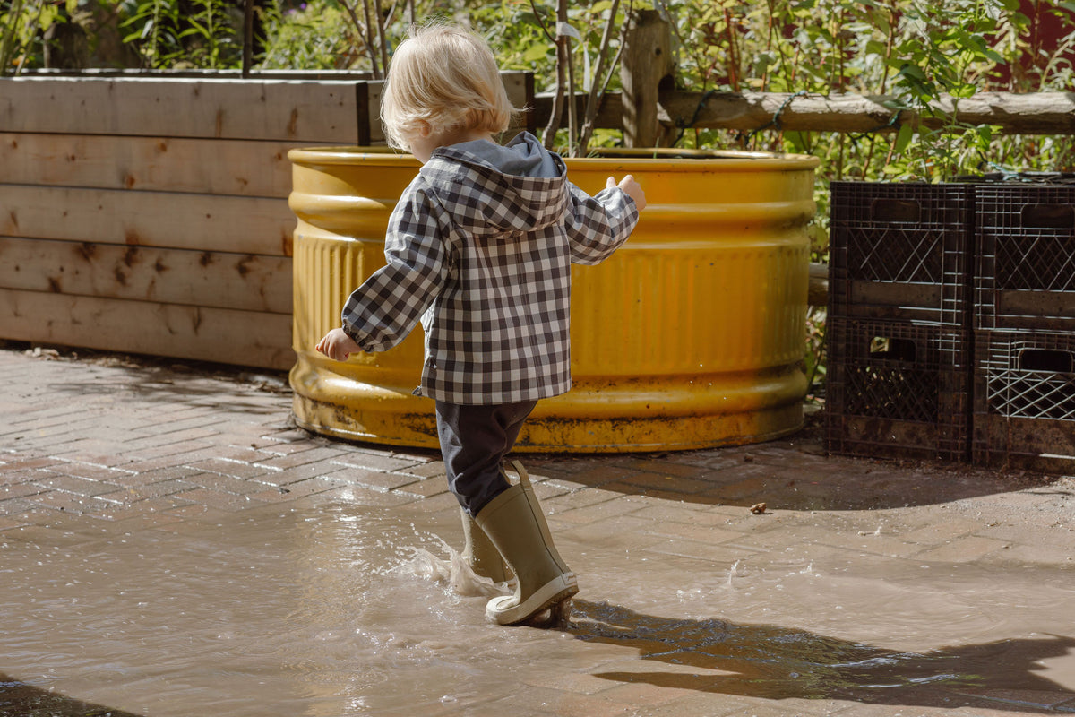 A horizontal image of a boy wearing the Park Jacket and Explorer Boots in a puddle.