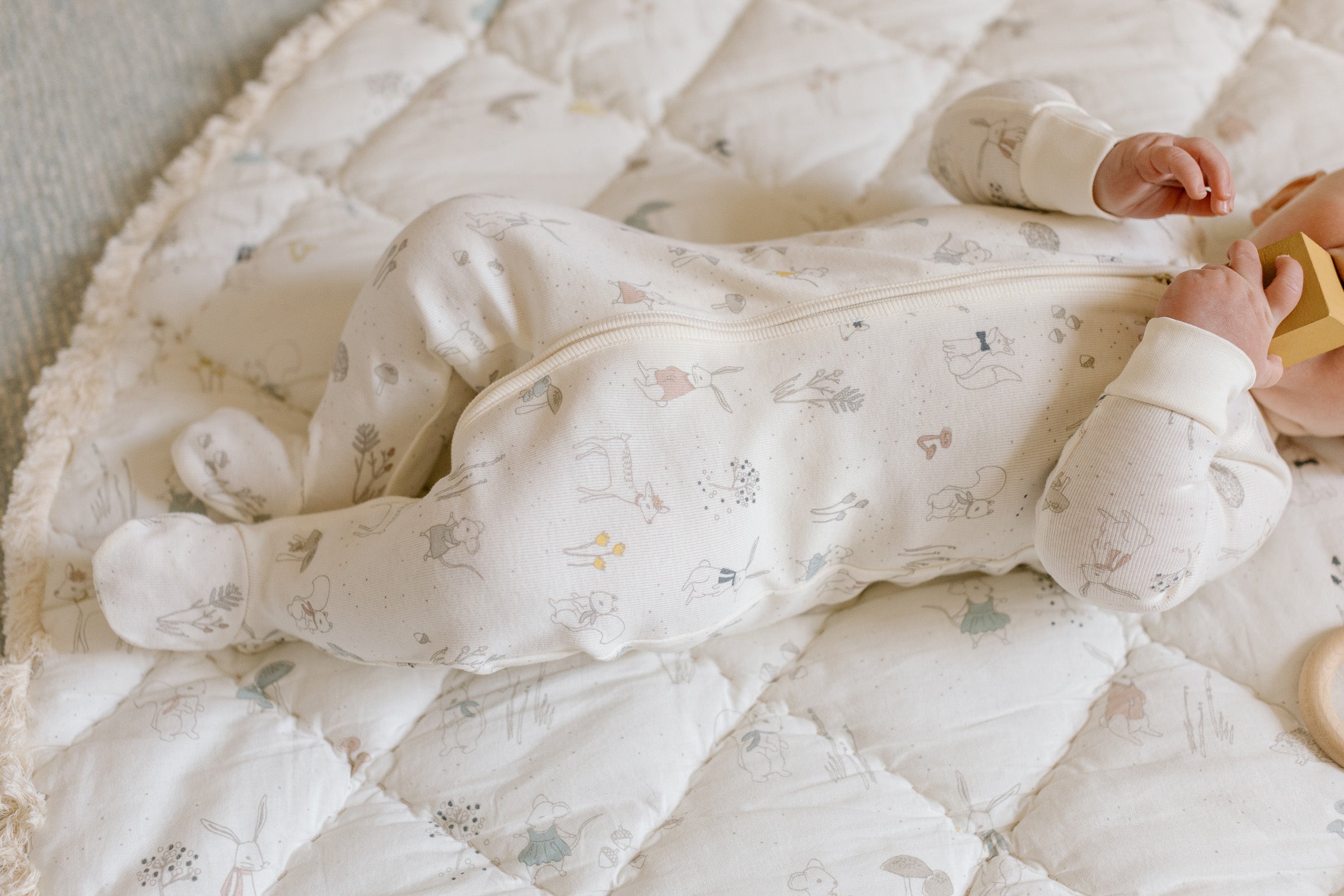 A baby lies on a play mat wearing a Pehr ribbed sleeper. 