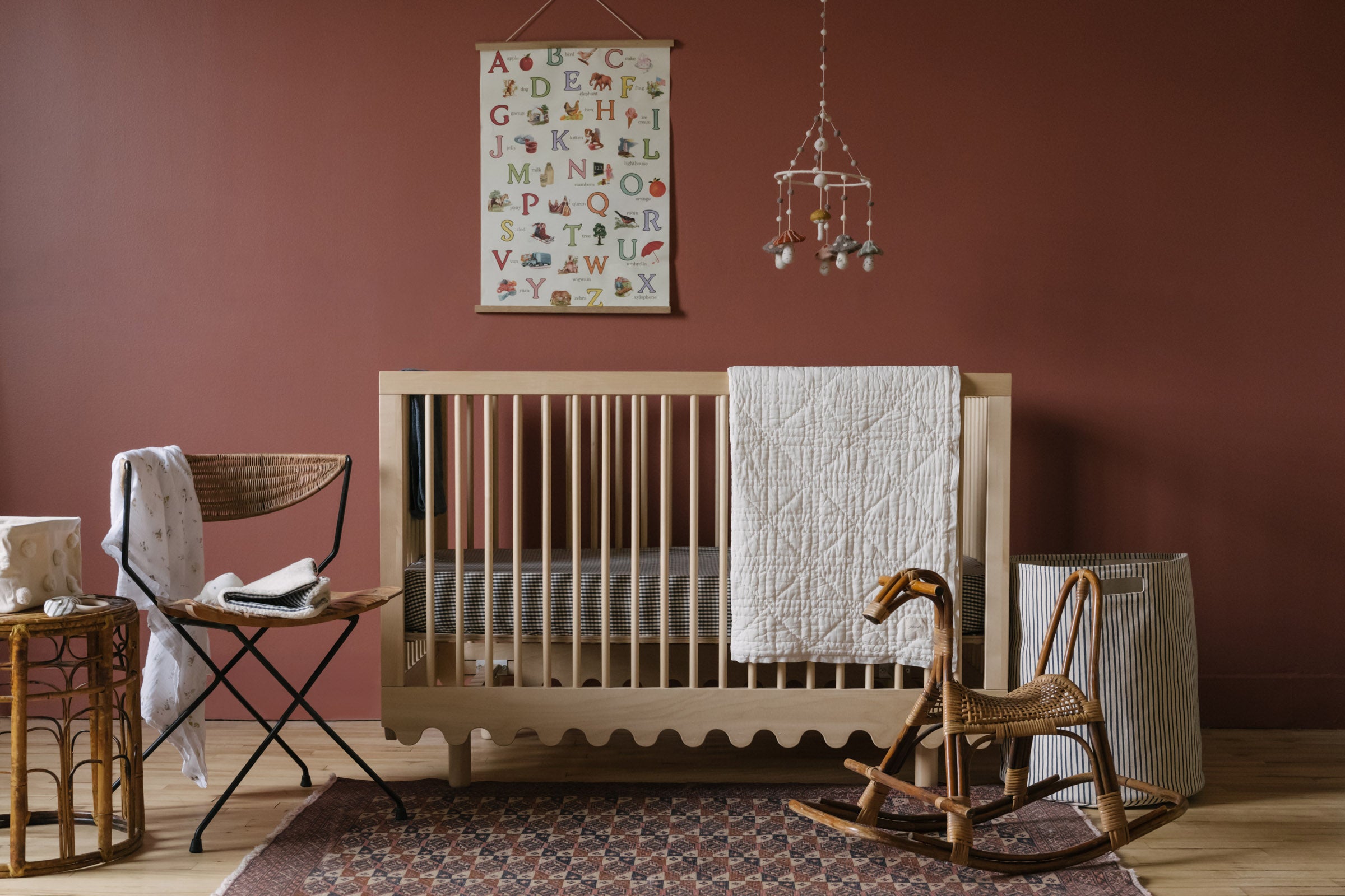 A fall nursery with mobile, blanket, gingham crib sheet and hamper