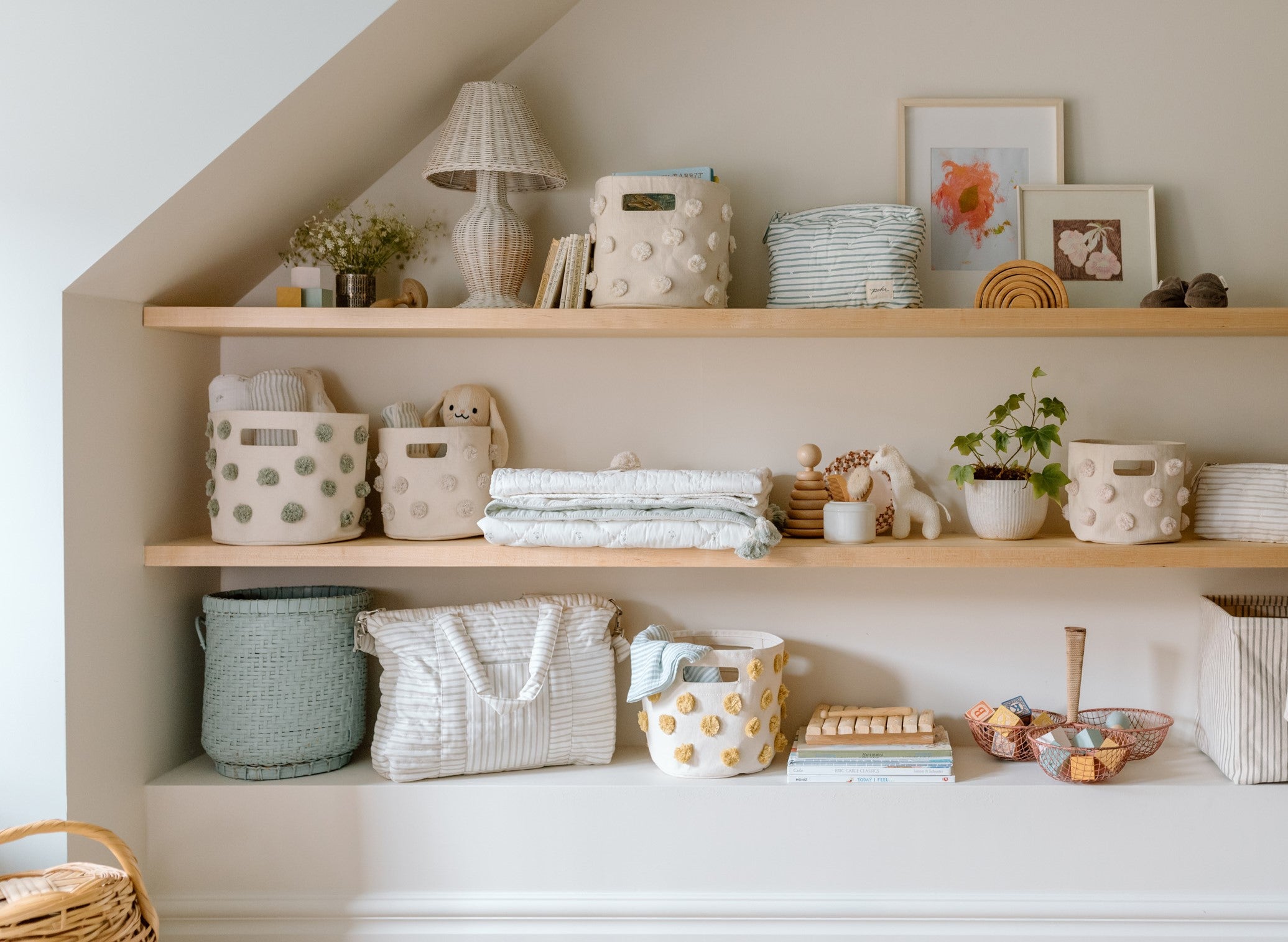 A horizontal image of a nursery wall with shelves containing pom pom storage, books, toys and other essentials.