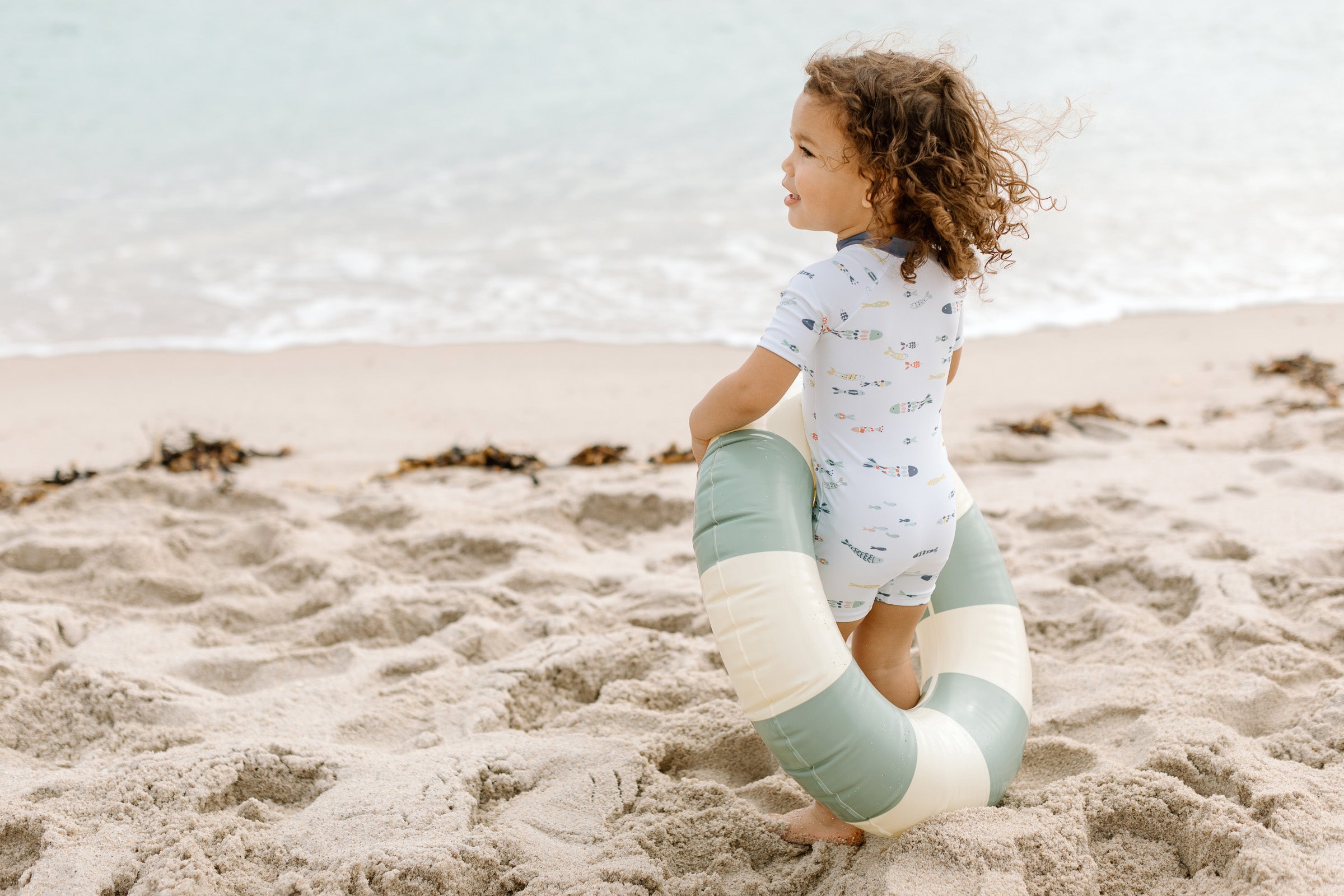 Little girl on a beach in a swim romper having fun with a beach toy