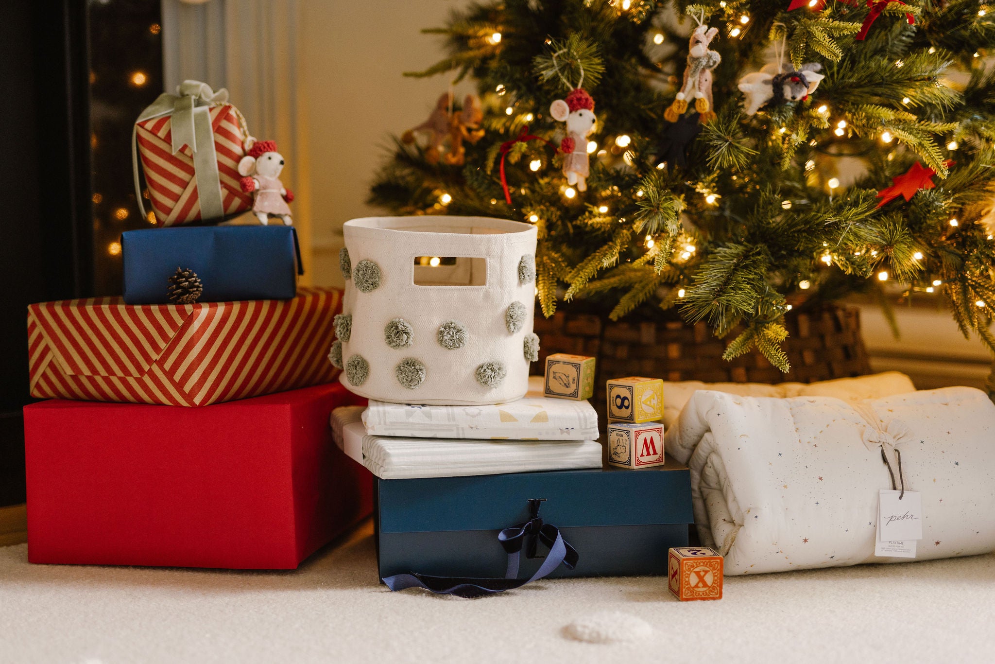 An image of a Christmas tree with gifts in front of it, including a pom pom mini and play mats.