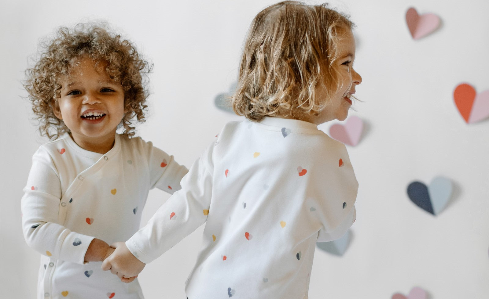 A little boy and girl dance in front of a backdrop with cut-out hearts.