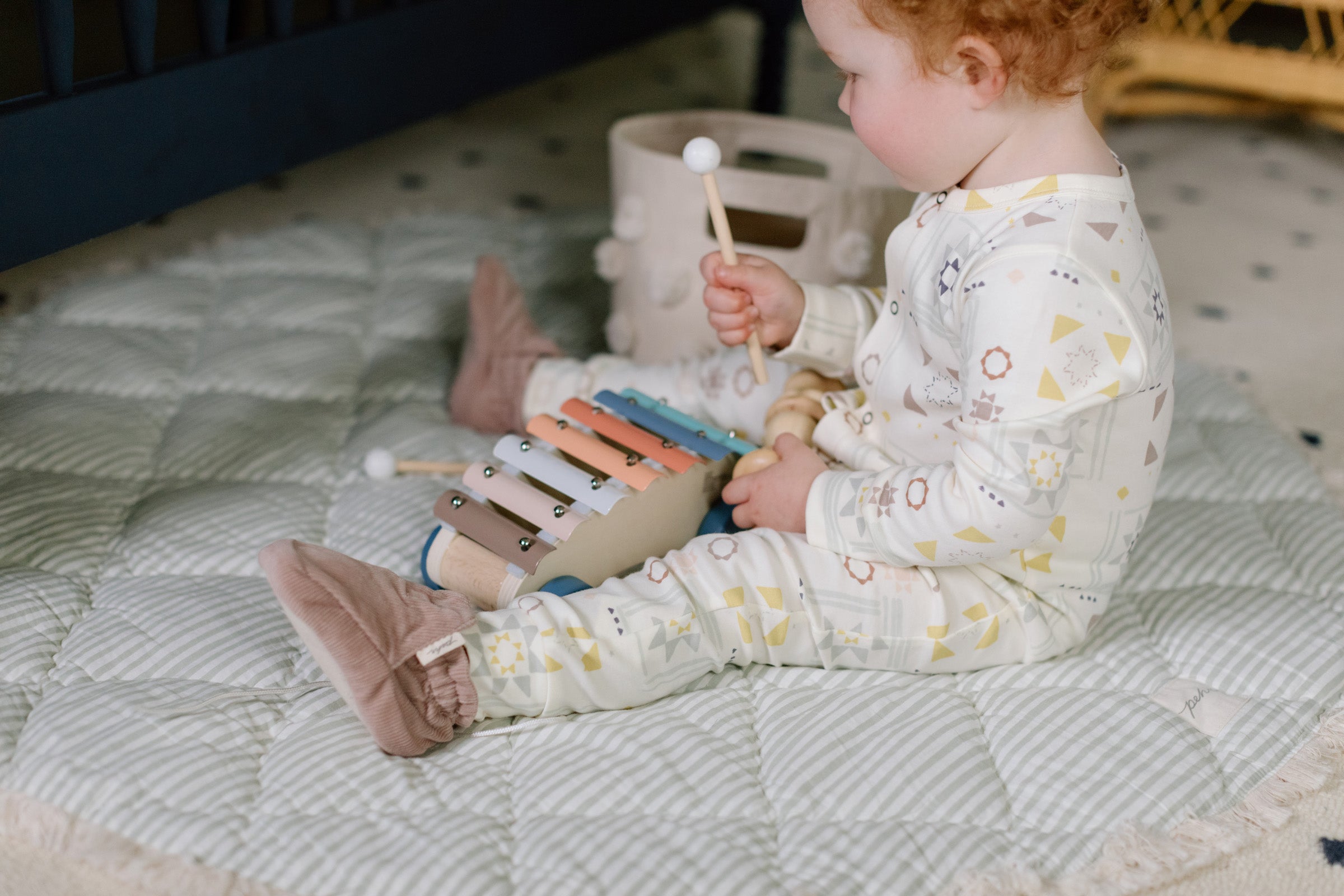 Horizontal image of a child sitting on a Pehr play mat in an organic cotton romper. 