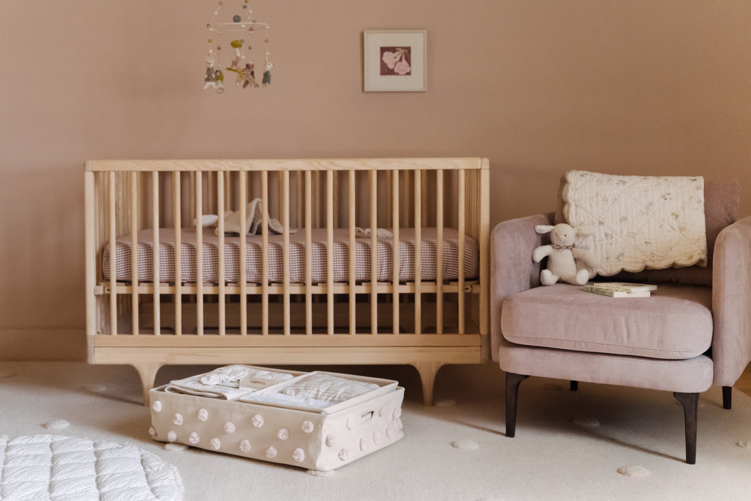 Image of baby nursery with crib, pink walls, pink velvet chair and Pehr Pom Pom Storage and Mobile