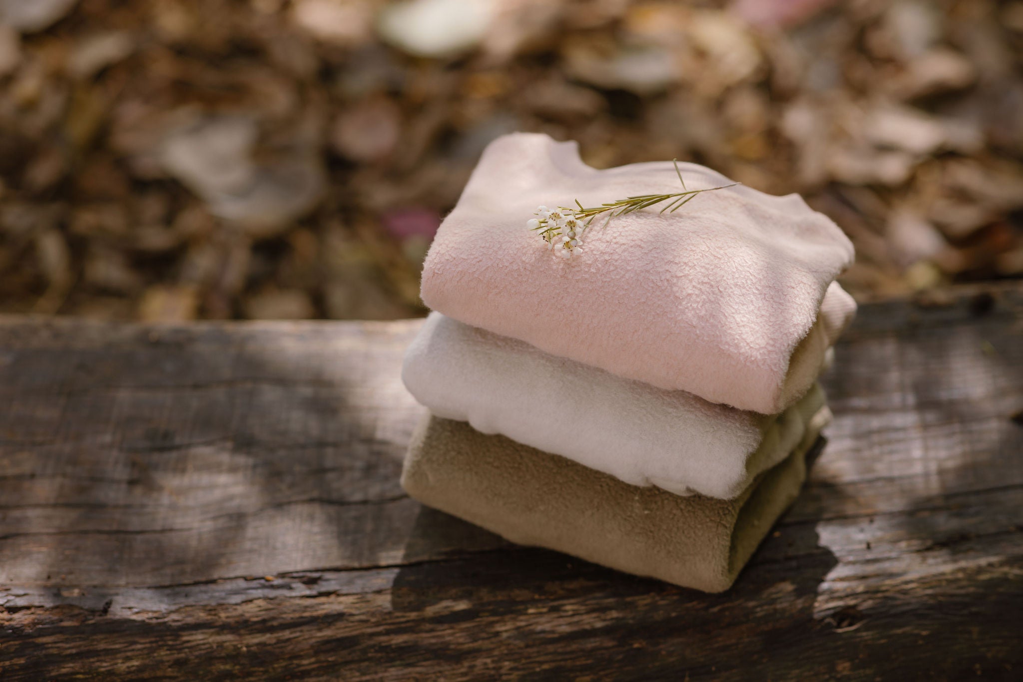 Stack of sweatshirts folded on a bench outside surrounded by leaves